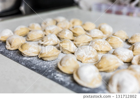 Raw homemade dumplings arranged on a floured board in the kitchen. Traditional cooking process before boiling. Close-up of uncooked pelmeni 131712802