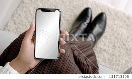 Woman holds smartphone mockup while sitting on sofa in cozy living room 131713106