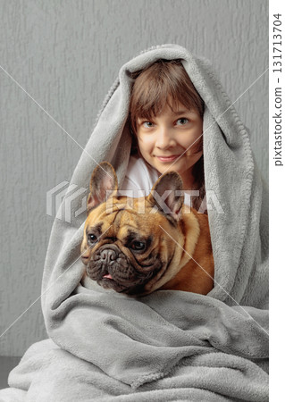 Girl and a French bulldog wrapped in a gray blanket. Girl and a French bulldog wrapped in a gray blanket. 131713704