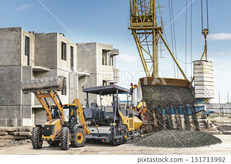 Construction site activity with heavy machinery pouring gravel into a foundation during daylight 131713992