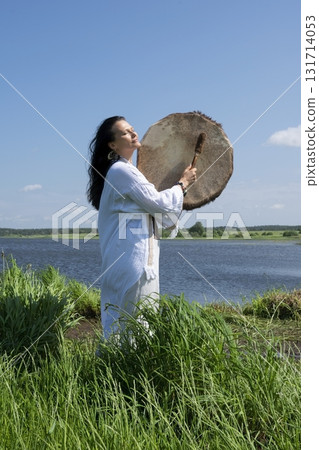 Female shaman drumming in the natural environment 131714053