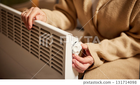 Woman adjusting power level on electric heater in warm home interior 131714098