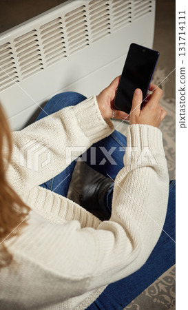 Woman using smartphone near electric heater in modern cozy room Woman using smartphone near electric heater in modern cozy room 131714111