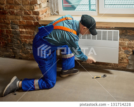 Technician installing white electric convector heater on brick wall indoors Technician installing white electric convector heater on brick wall indoors 131714228