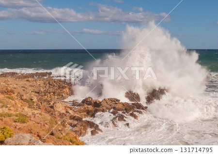 Stormy seascape with waves crashing against rocky shore and high white foam splashes. 131714795