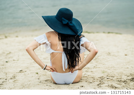 A young girl is lying on the sandy beach, emphasizing the beauty of her white swimsuit 131715143