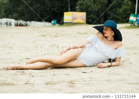 A young girl is lying on the sandy beach, emphasizing the beauty of her white swimsuit A young girl is lying on the sandy beach, emphasizing the beauty of her white swimsuit 131715144