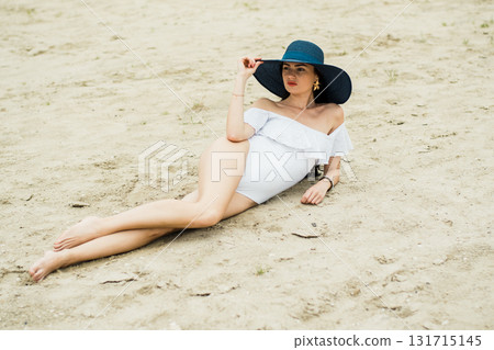 A young girl is lying on the sandy beach, emphasizing the beauty of her white swimsuit A young girl is lying on the sandy beach, emphasizing the beauty of her white swimsuit 131715145