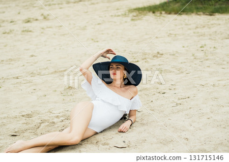 A beautiful woman in a white swimsuit is resting on the golden sand, creating a feeling of summer comfort A beautiful woman in a white swimsuit is resting on the golden sand, creating a feeling of summer comfort 131715146