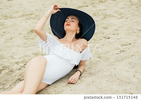 A beautiful woman in a white swimsuit is resting on the golden sand, creating a feeling of summer comfort A beautiful woman in a white swimsuit is resting on the golden sand, creating a feeling of summer comfort 131715148