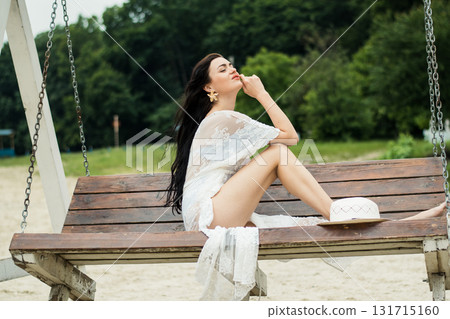A girl with long black hair sits on a swing in the middle of a sandy beach A girl with long black hair sits on a swing in the middle of a sandy beach 131715160