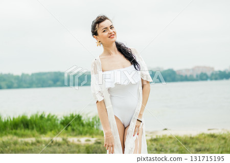A young woman with long black hair is standing against the background of a summer landscape A young woman with long black hair is standing against the background of a summer landscape 131715195