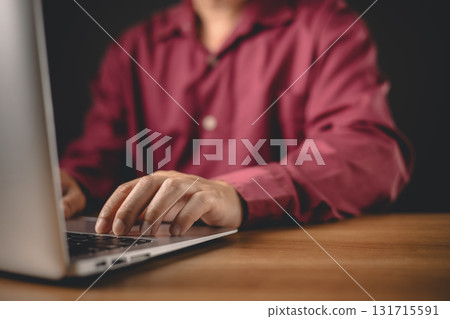 A person in a maroon shirt types on a laptop at a wooden desk, symbolizing focus, productivity, and digital work in a modern setting without distractions or external influences. A person in a maroon shirt types on a laptop at a wooden desk, symbolizing focus, productivity, and digital work in a modern setting without distractions or external influences. 131715591