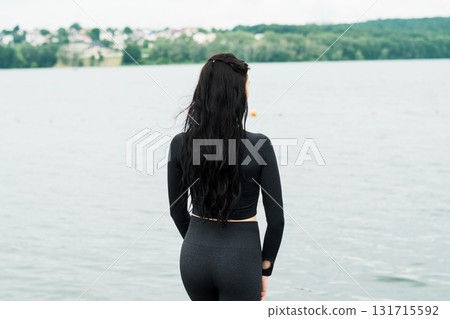 A girl wearing black leggings and a tight sweatshirt is performing gymnastic exercises on the shore of a lake A girl wearing black leggings and a tight sweatshirt is performing gymnastic exercises on the shore of a lake 131715592