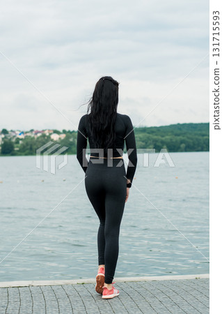 A girl wearing black leggings and a tight sweatshirt is performing gymnastic exercises on the shore of a lake A girl wearing black leggings and a tight sweatshirt is performing gymnastic exercises on the shore of a lake 131715593