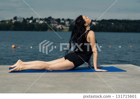 A woman with an athletic build performs gymnastics exercises by the lake A woman with an athletic build performs gymnastics exercises by the lake 131715601