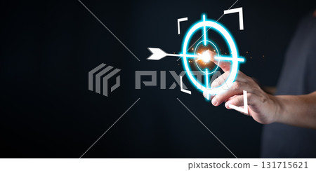 A person in a dark shirt touches a glowing virtual bullseye with an arrow hitting the center, symbolizing target precision, focus, clear goal, defined mission, and purposeful purpose driven strategy. 131715621