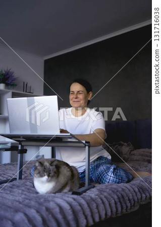 a senior woman works from home on a laptop with a pet, a cat 131716038