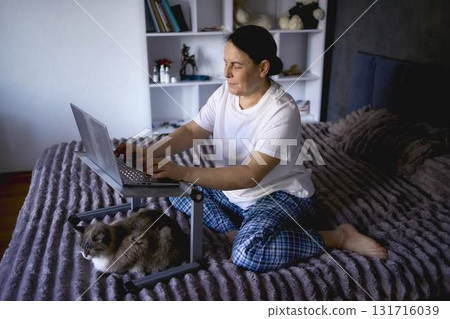 a senior woman works from home on a laptop with a pet, a cat a senior woman works from home on a laptop with a pet, a cat 131716039
