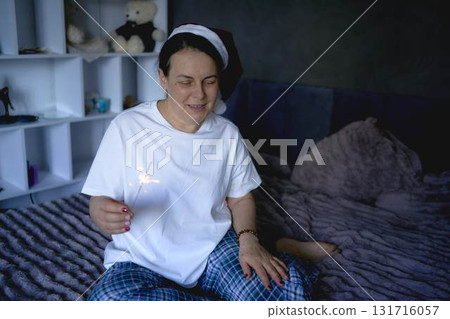 a senior woman in a Santa Claus hat and with a sparkler on a video conference wishes everyone a Merry Christmas at home via the Internet a senior woman in a Santa Claus hat and with a sparkler on a video conference wishes everyone a Merry Christmas at home via the Internet 131716057