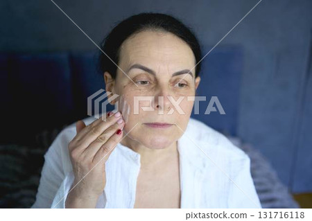 a       senior woman in underwear on the bed performs routine self-care with face and body cosmetics, face foam 131716118