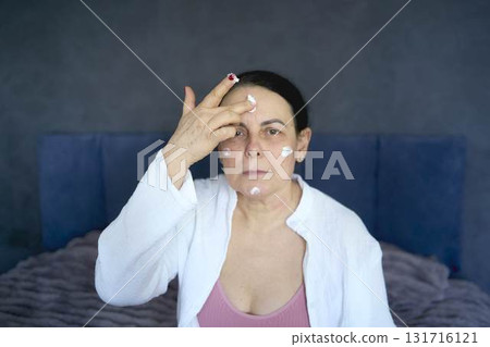 a senior woman in underwear on the bed performs routine self-care with face and body cosmetics 131716121
