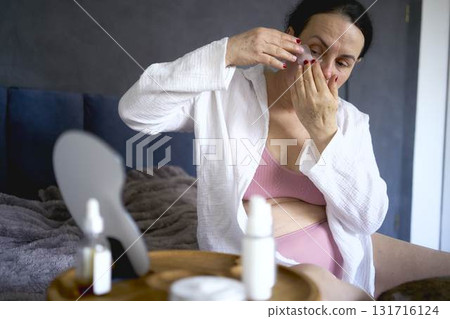 a senior woman in underwear on the bed performs routine self-care with face and body cosmetics, patches under the eyes a senior woman in underwear on the bed performs routine self-care with face and body cosmetics, patches under the eyes 131716124