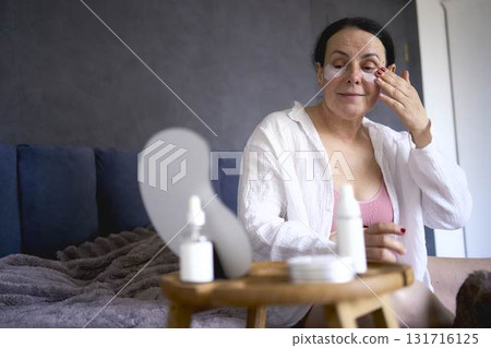 a senior woman in underwear on the bed performs routine self-care with face and body cosmetics, patches under the eyes a senior woman in underwear on the bed performs routine self-care with face and body cosmetics, patches under the eyes 131716125