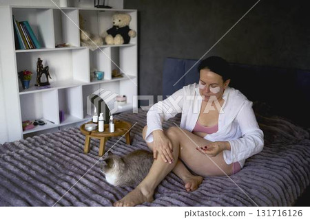 a senior woman in underwear on the bed performs routine self-care with body cosmetics 131716126