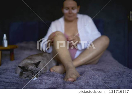 a senior woman in underwear on the bed performs routine self-care with body cosmetics a senior woman in underwear on the bed performs routine self-care with body cosmetics 131716127