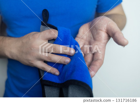 A man suffers from palmar hyperhidrosis. He wipes his sweaty palms due to excessive sweating. Treatment of hyperhidrosis with botulinum toxin injection into the hand. A man suffers from palmar hyperhidrosis. He wipes his sweaty palms due to excessive sweating. Treatment of hyperhidrosis with botulinum toxin injection into the hand. 131716186
