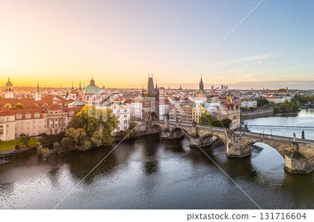 Stunning view of Old Town Bridge Tower at Charles Bridge during sunset. The serene Vltava River reflects the historic architecture of Prague, creating a picturesque scene. 131716604