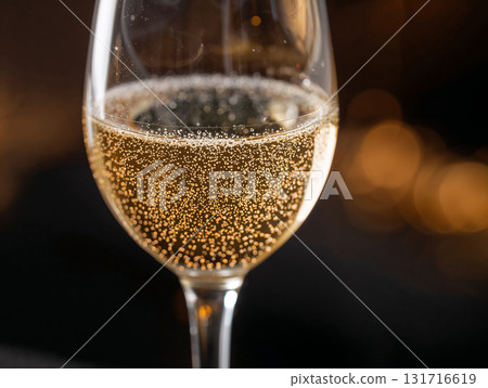 Close-up of a glass of sparkling champagne with bubbles. A festive drink for a party, celebration, or special occasion. Golden bokeh lights in a restaurant or bar background. 131716619