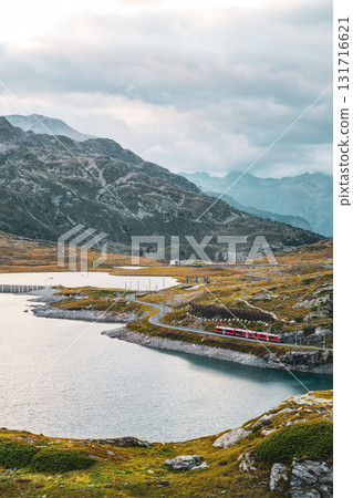 Lago Bianco, nestled in the Bernina Pass, showcases stunning alpine scenery during the evening. The tranquil lake reflects the surrounding mountain peaks and passes. 131716621
