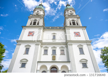 St. Lorenz Basilica stands majestically in Kempten, Bavaria, showcasing its baroque architecture against a backdrop of blue skies. Tourists admire the detailed design and serene surroundings. St. Lorenz Basilica stands majestically in Kempten, Bavaria, showcasing its baroque architecture against a backdrop of blue skies. Tourists admire the detailed design and serene surroundings. 131716640