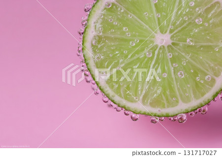 A fresh lime slice rests against a pink background, featuring tiny bubbles clinging to its surface. The vibrant green color of the lime stands out, creating a refreshing look. 131717027