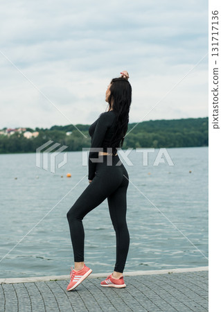 A beauty in a black sports kit is practicing yoga on the beach by the lake 131717136
