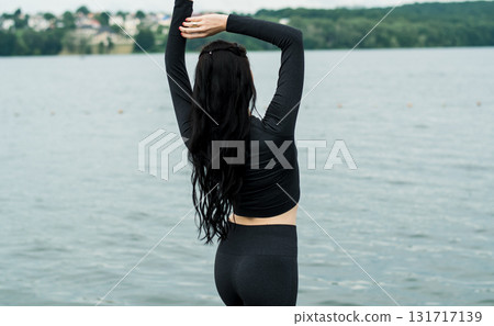 A young woman in dark sportswear is practicing gymnastics on the beach A young woman in dark sportswear is practicing gymnastics on the beach 131717139