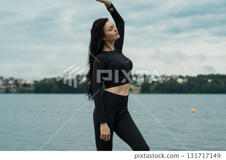 A beautiful woman with an athletic build poses against the backdrop of the water's surface 131717149