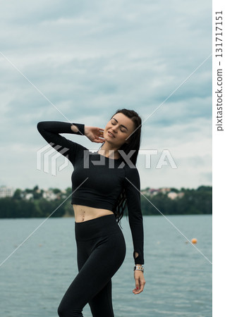 A beautiful woman with an athletic build poses against the backdrop of the water's surface A beautiful woman with an athletic build poses against the backdrop of the water's surface 131717151