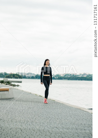 An athletic girl runs along the lake in black leggings and a tight-fitting shirt 131717161