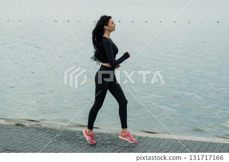 A young woman with an athletic build jogs against the backdrop of a lake landscape A young woman with an athletic build jogs against the backdrop of a lake landscape 131717166