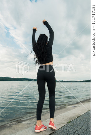 A woman with long dark hair in black leggings stands by clear water A woman with long dark hair in black leggings stands by clear water 131717182