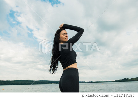 An athlete with an athletic build poses in black clothing against the backdrop of a natural landscape An athlete with an athletic build poses in black clothing against the backdrop of a natural landscape 131717185