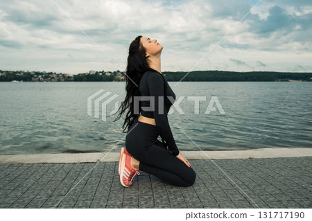 A young girl in a black sports outfit is standing by the lake A young girl in a black sports outfit is standing by the lake 131717190