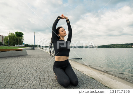 A woman with a slender athletic build performs gymnastics exercises against the backdrop of a lake 131717196