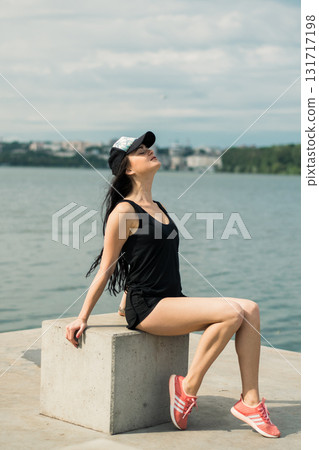 A young girl with an athletic build sits on the shore of a lake, enjoying the silence A young girl with an athletic build sits on the shore of a lake, enjoying the silence 131717198
