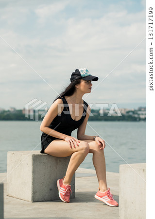 A young girl with an athletic build sits on the shore of a lake, enjoying the silence 131717199
