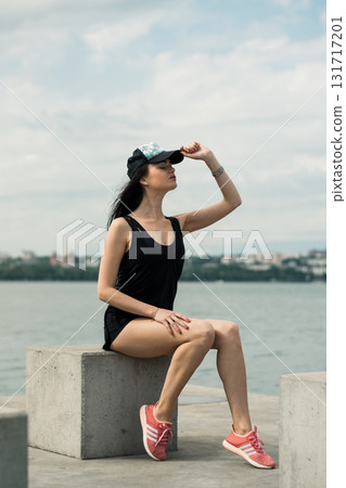 A slender athlete sits by the calm water A slender athlete sits by the calm water 131717201