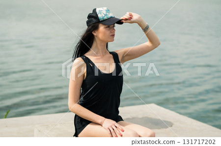 A slender athlete sits by the calm water A slender athlete sits by the calm water 131717202